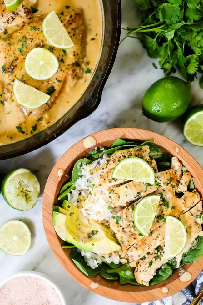 This Paleo and Whole30 friendly coconut lime chicken is so flavorful, fresh and satisfying! Coconut lime chicken in a bowl with spinach, rice, avocado and lime wedges and cilantro on top.