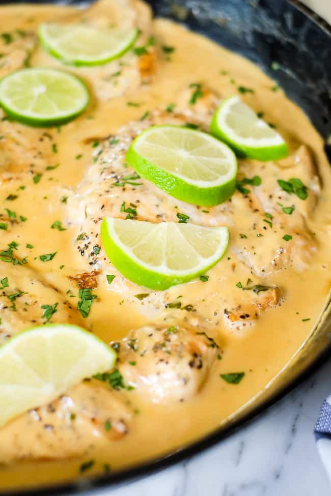 This Paleo and Whole30 friendly coconut lime chicken is so flavorful, fresh and satisfying! Coconut lime chicken in cast iron skillet with lime wedges and cilantro on top. 