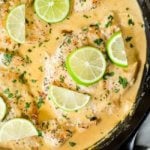 Coconut lime chicken with a creamy light orange sauce in a cast iron skillet with lime wedges and chopped cilantro on top