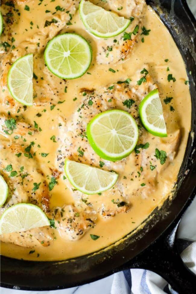 Coconut lime chicken with a creamy light orange sauce in a cast iron skillet with lime wedges and chopped cilantro on top
