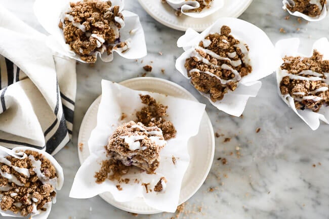 Horizontal overhead image of coffee cake muffins spread out on marble. Some on marble, some on plates. Drizzled with coconut butter on top. 