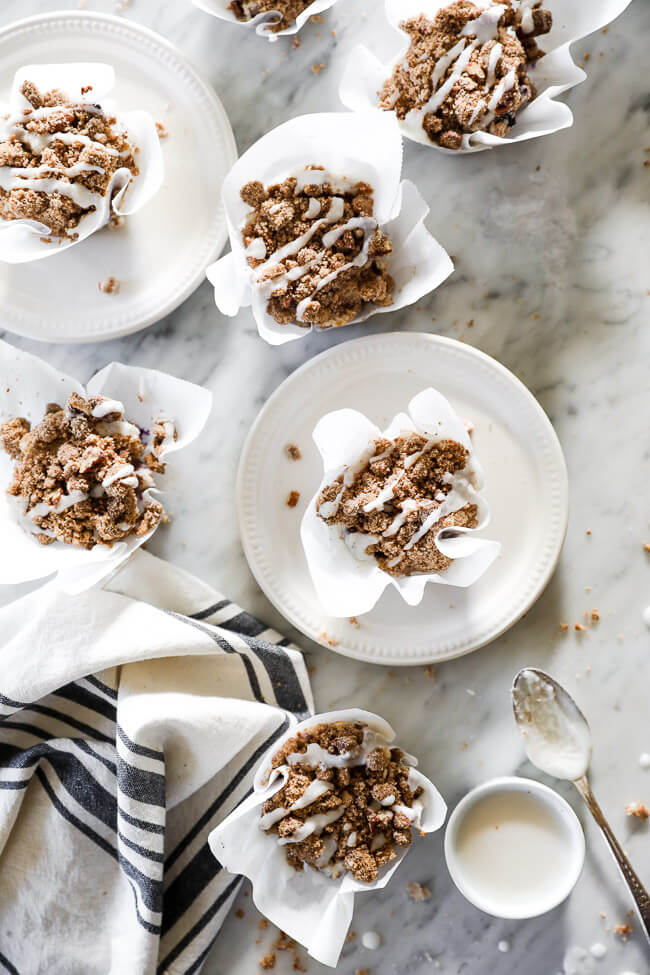 Overhead vertical image of coffee cake muffins spread out on marble. Some on plates and some on marble. Extra coconut butter on the side with a spoon. 