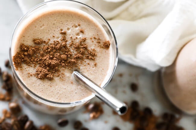 Horizontal overhead image of coffee smoothie in a glass with cacao sprinkled on top and a stainless steel straw. 