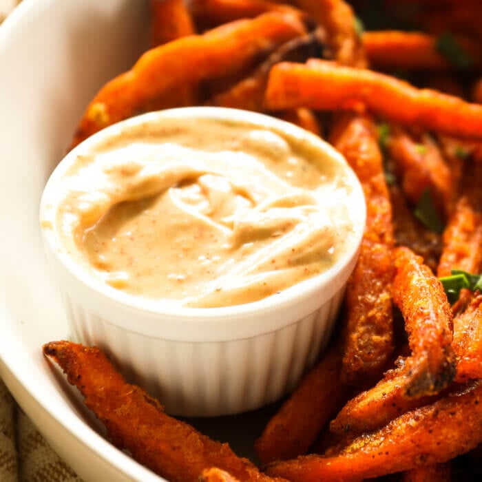 Close up angle image of sweet potato fries dipping sauce in a ramekin with a bowl of fries