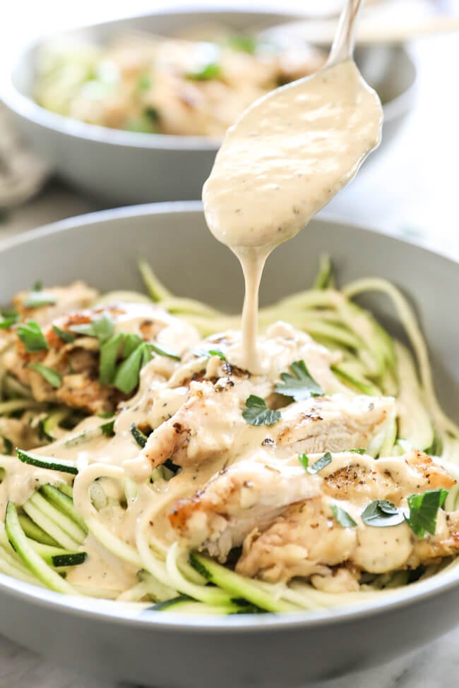 Vertical angled shot of spooning alfredo sauce over chicken and zucchini noodles. 