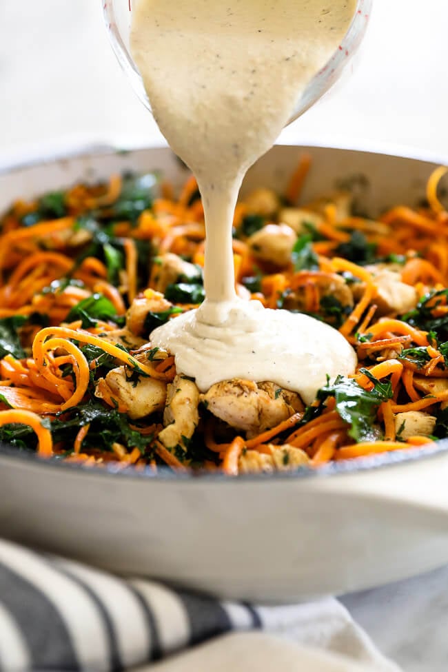 Pouring sauce on chicken sweet potato noodles in pan vertical image