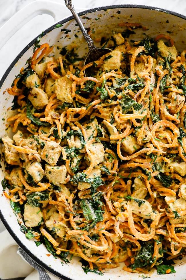 Overhead shot of creamy chicken sweet potato noodles in a pan with spoon at top vertical image