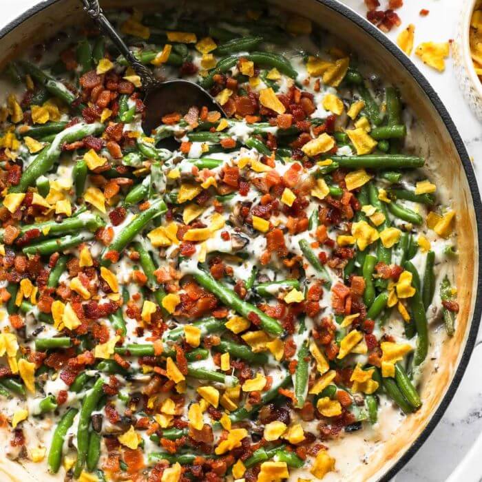 Close up overhead image of a skillet with green beans, a dairy free cream of mushroom sauce, crumbled bacon and plantain chips on top.