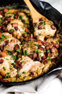 Close up angle image of creamy garlic chicken thighs in a cast iron skillet with chopped bacon and parsley on top