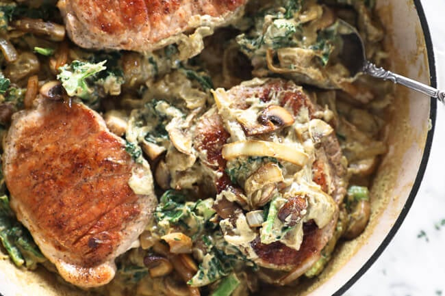 Horizontal overhead image of creamy pork chops in a skillet with a serving spoon. 