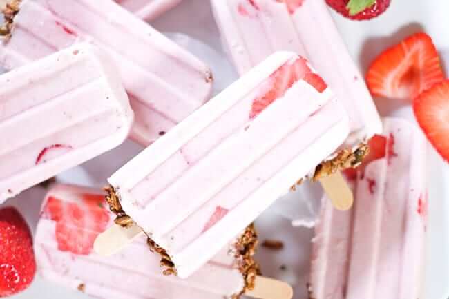 Creamy strawberry popsicles with granola on the bottom and fresh strawberries