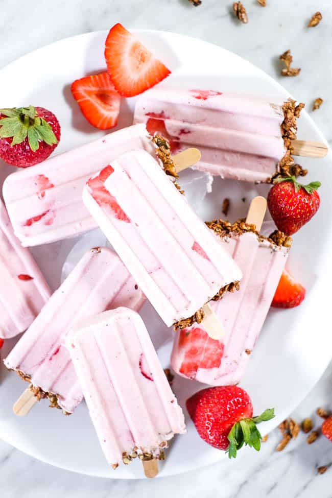 Creamy strawberry popsicles with granola on the bottom and fresh strawberries on a plate.