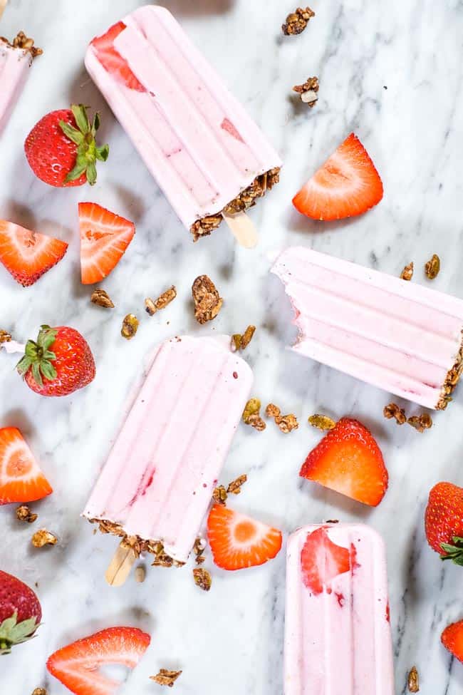 Creamy strawberry popsicles with granola on the bottom and fresh strawberries
