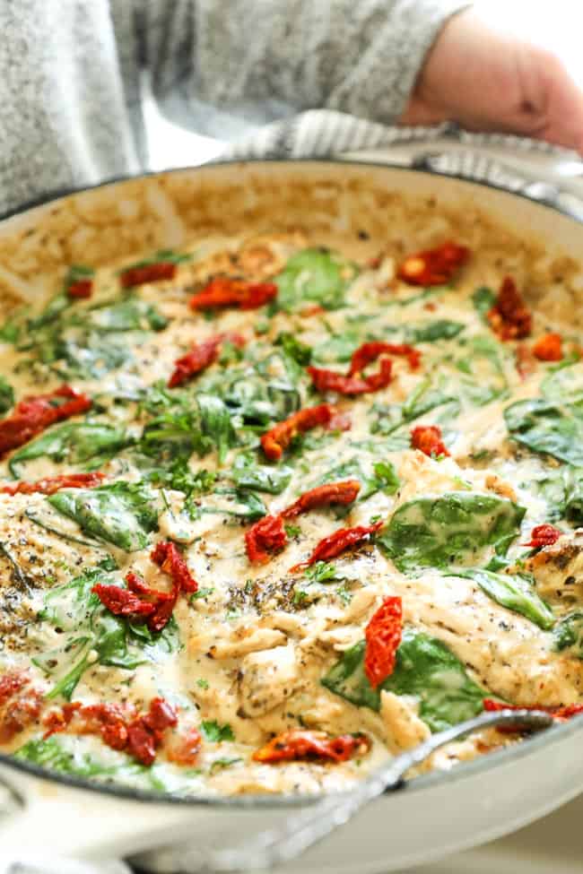 Creamy tuscan chicken in skillet someone holding skillet