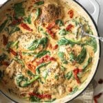Close up overhead image of creamy tuscan chicken in a skillet with fresh herbs, spinach and sundried tomatoes.
