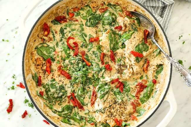 Horizontal image of creamy tuscan chicken in skillet with serving spoon in dish. Topped with more sun-dried tomatoes and fresh parsley.