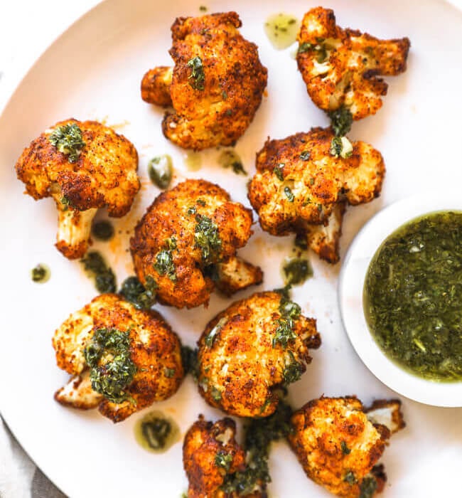 Crispy air fryer cauliflower on a white plate with chimichurri sauce ont top