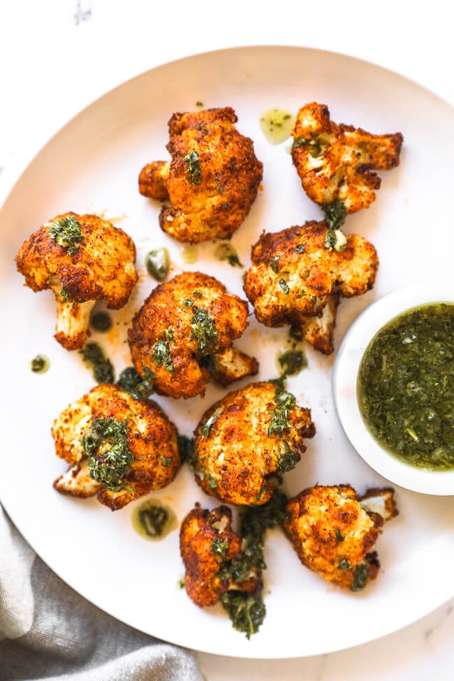 Crispy air fryer cauliflower on a white plate with chimichurri sauce ont top