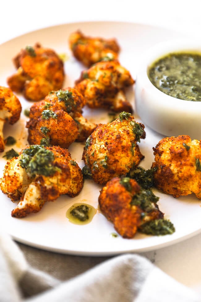 Close up angled image of air fryer cauliflower on a white plate with green sauce