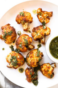 Crispy air fryer cauliflower on a white plate with green sauce on top and on the side