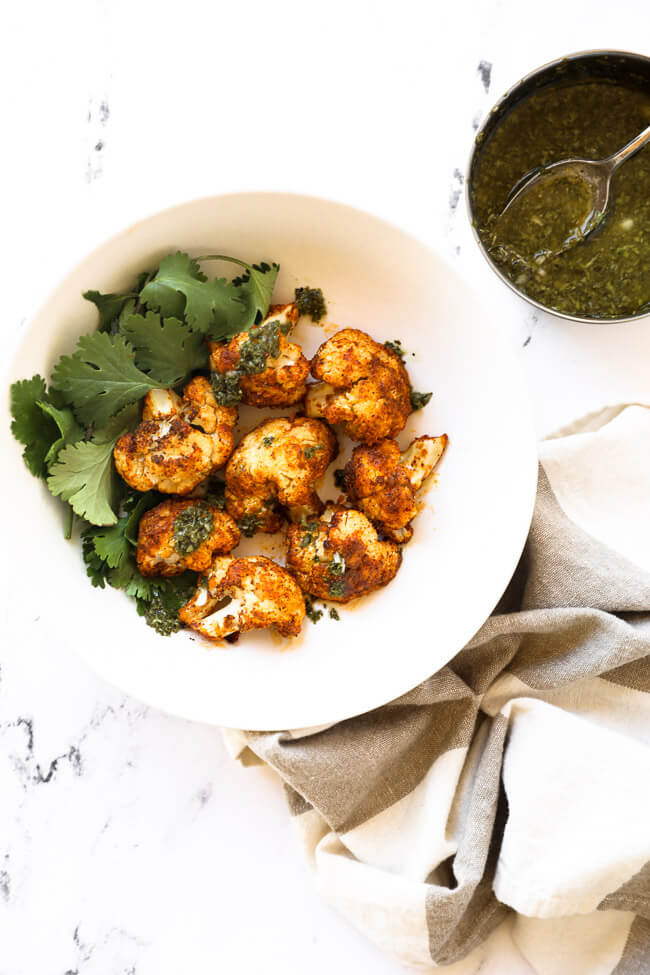 Bowl of air fryer cauliflower with parsley garnish and green sauce on the side