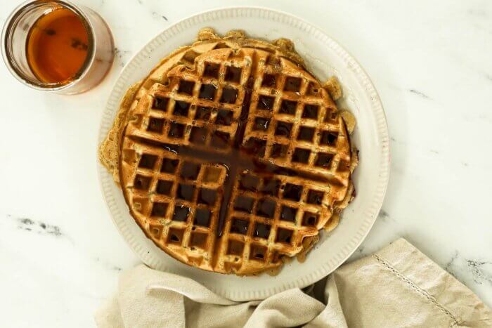 Image of cooked oat flour waffles on a plate with maple syrup on top.