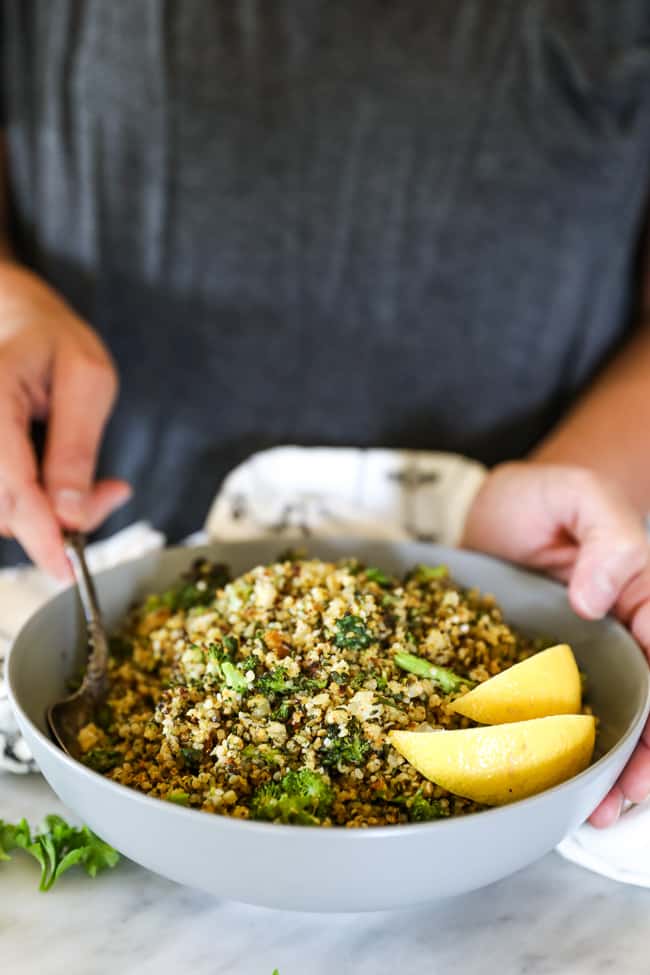 Holding a bowl of crispy roasted cauliflower rice with lemon wedges in it and scooping some out. 