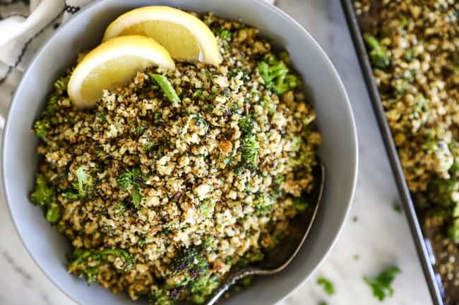 Crispy roasted cauliflower rice in a serving bowl with a spoon and lemon wedges. 