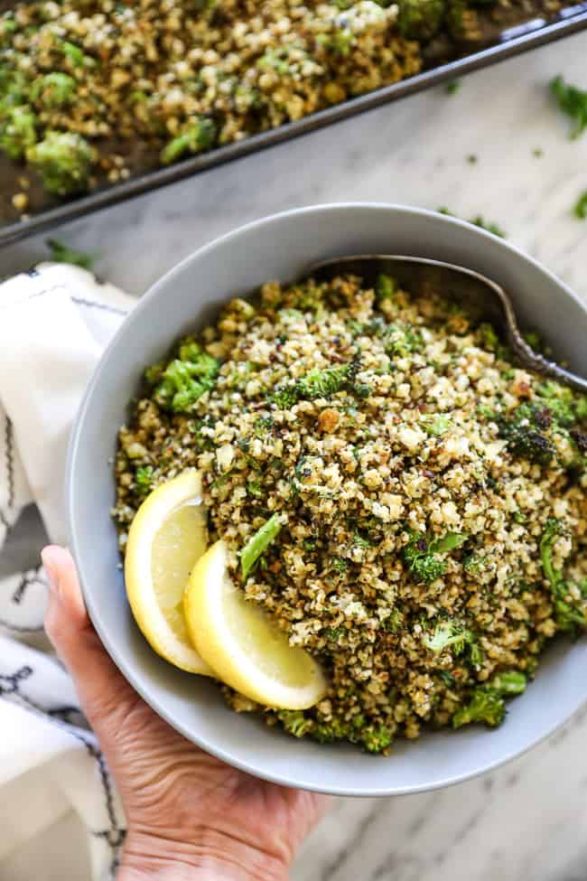 Holding a bowl of crispy roasted cauliflower rice with a serving spoon and lemon wedges in it. 