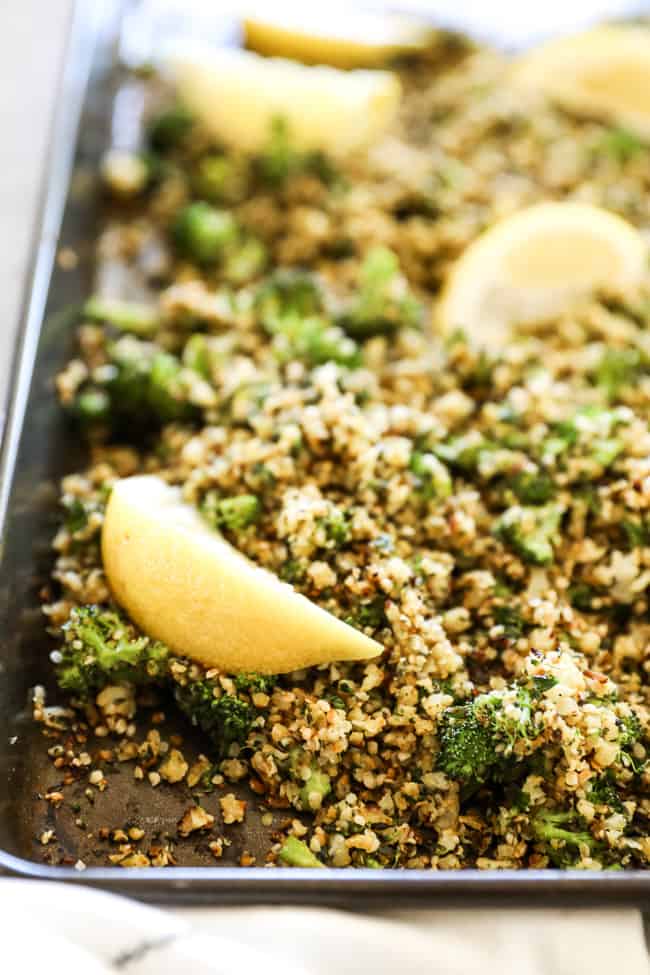 Crispy roasted cauliflower rice on a sheet pan with lemon wedges spread about. 