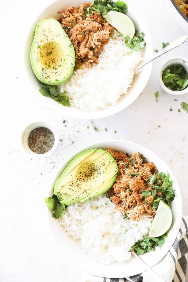 Vertical overhead image of two bowls with mexican chicken, rice and avocado. Garnished with a lime wedge and and fresh cilantro. 