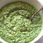 Close up angle of a bowl filled with pesto sauce and a spoon in bowl