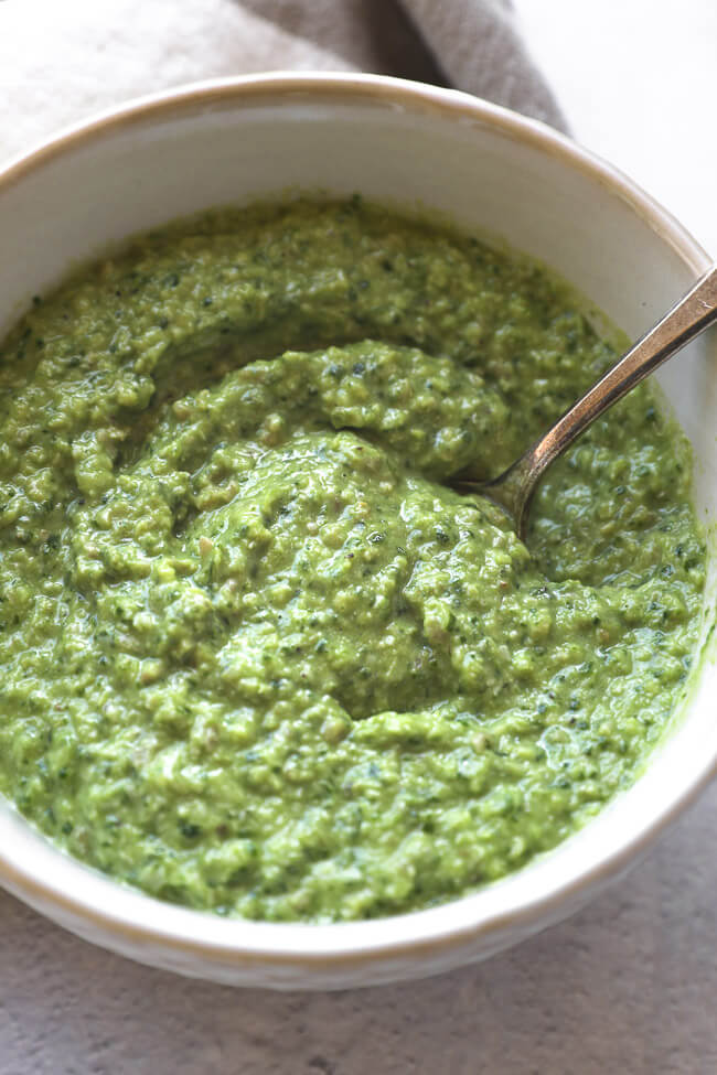 Overhead close up of dairy free and nut free pesto in a bowl with a spoon. 