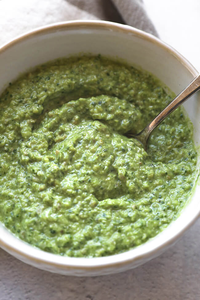 Close up angle of a bowl filled with pesto sauce and a spoon in bowl