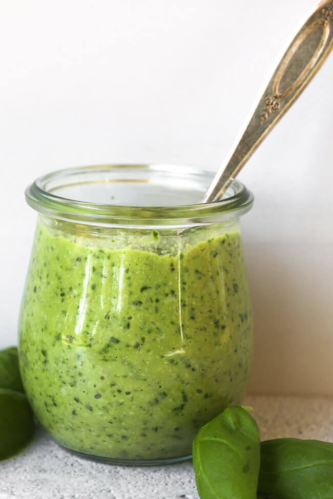 Straight on image of a small canister with dairy free and nut free pesto and spoon in it. 