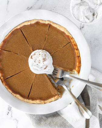 Dairy free and gluten free pumpkin pie in pie dish with whipped coconut cream on top. One slice of pie missing from dish and two forks dug into the missing spot.