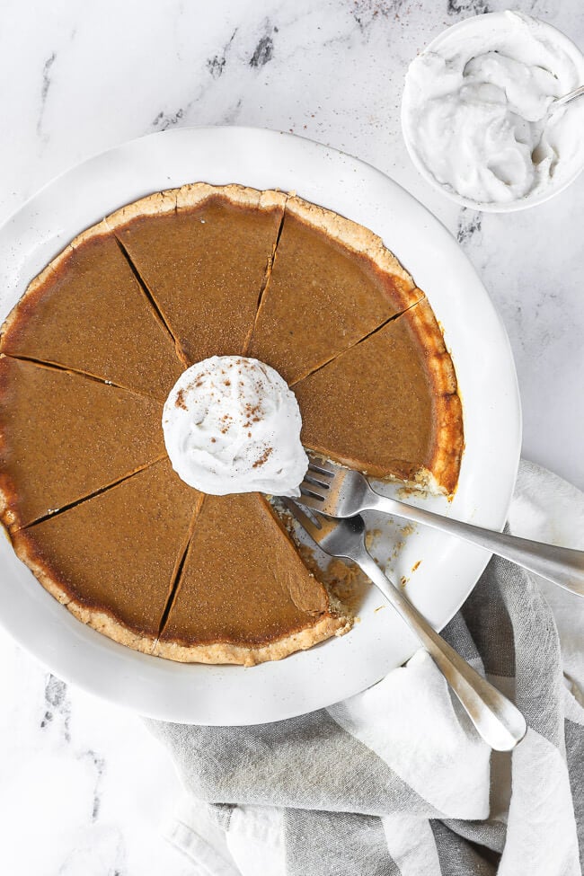 Dairy free and gluten free pumpkin pie in pie dish with whipped coconut cream on top. One slice of pie missing from dish and two forks dug into the missing spot.