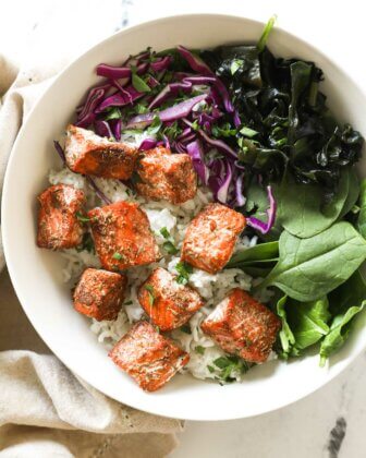 Cooked salmon bites over rice, greens and purple cabbage in a bowl