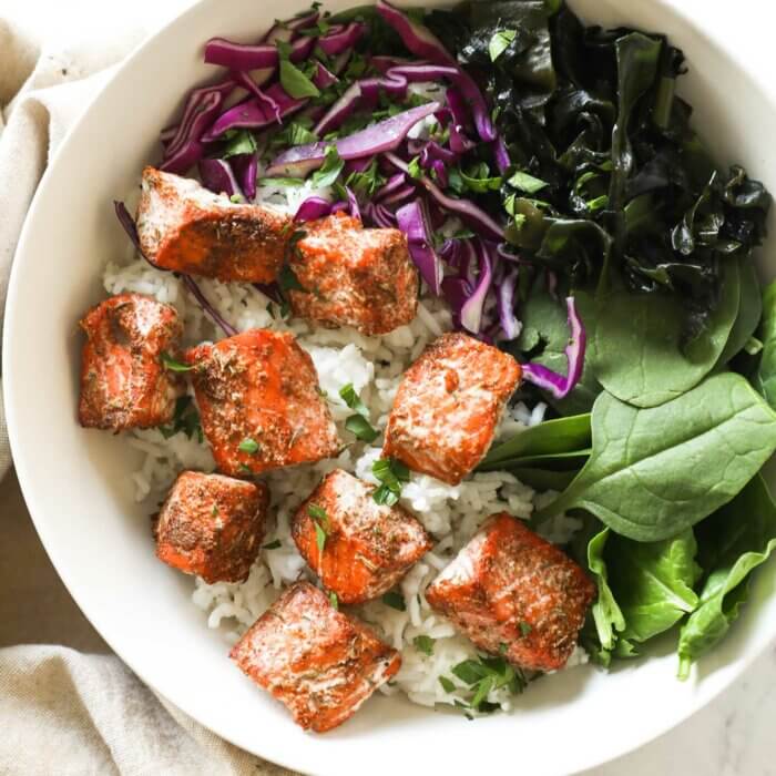 Cooked salmon bites over rice, greens and purple cabbage in a bowl