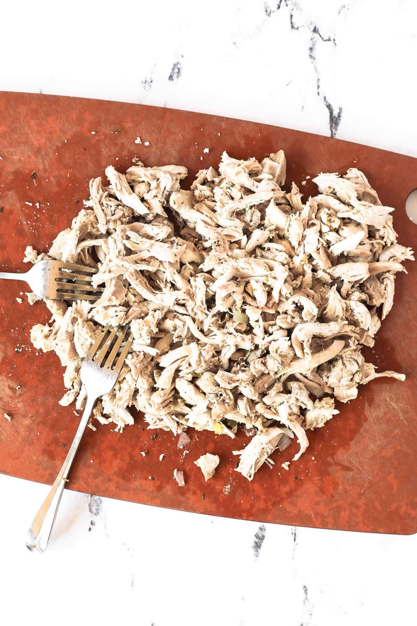 Shredded chicken on a cutting board after it cooked in the broth.