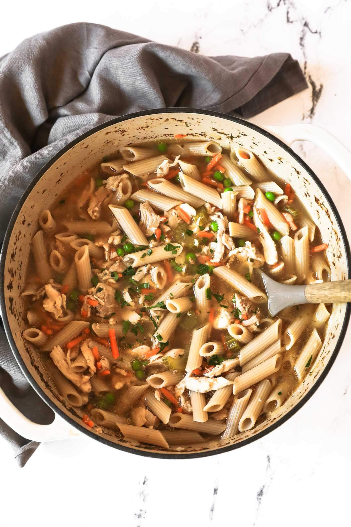 Overhead shot of chicken noodle soup in the big pot with a serving spoon and fresh parley sprinkled on top.