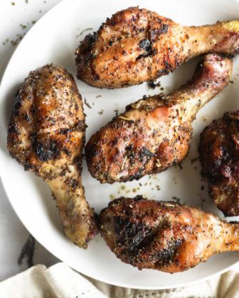 Close up overhead image of smoked chicken drumsticks on a white plate with seasoning sprinkled around