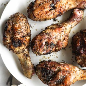 Close up overhead image of smoked chicken drumsticks on a white plate with seasoning sprinkled around