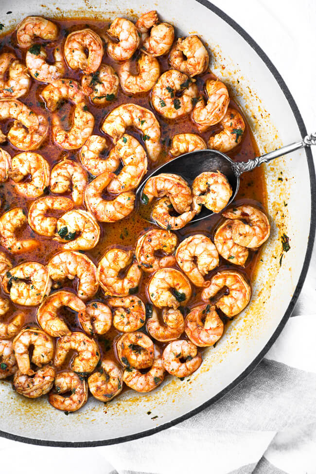 Overhead image of chili lime shrimp in a skillet with a serving spoon and chopped cilantro sprinkled on top. 