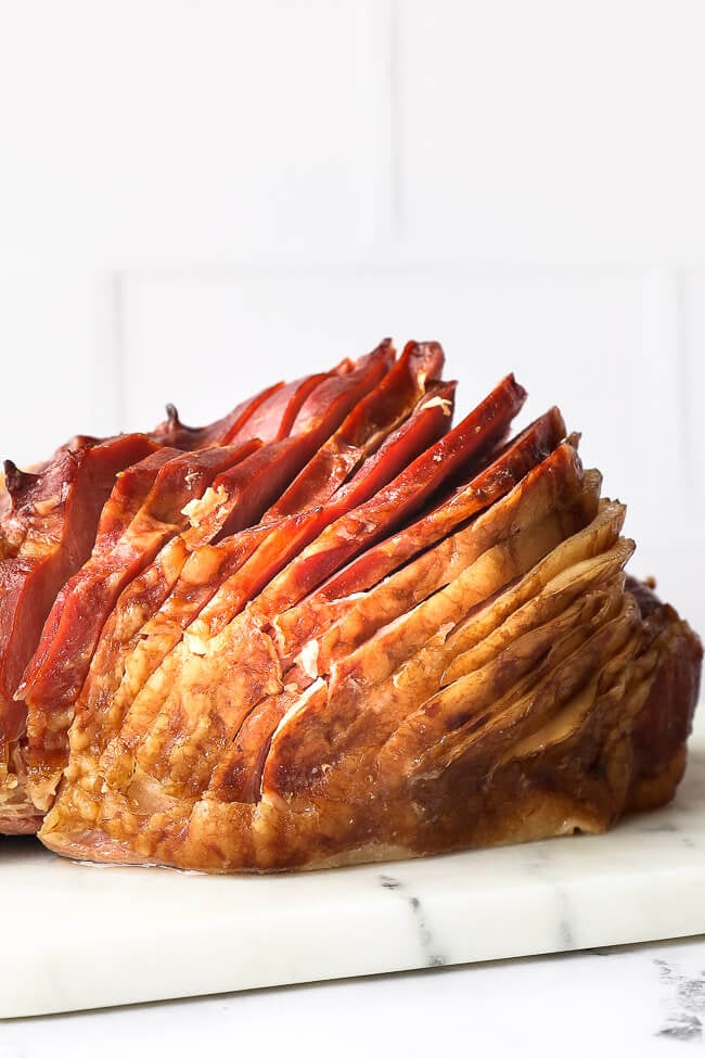 Close up straight on shot of whole ham with a thick spiral slice on a marble board 