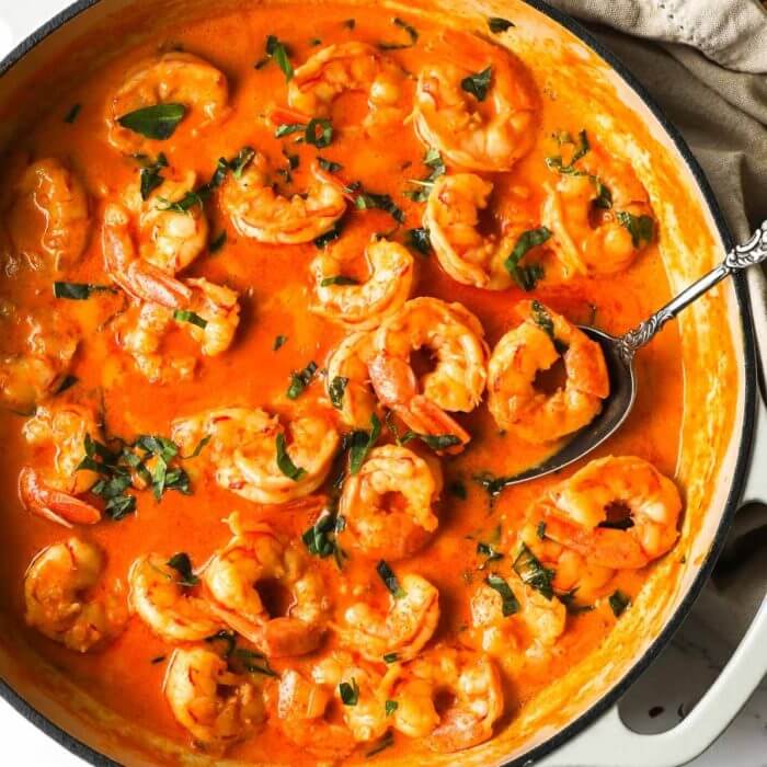 Overhead image of cooked creamy coconut shrimp in a pan with spoon and basil garnish