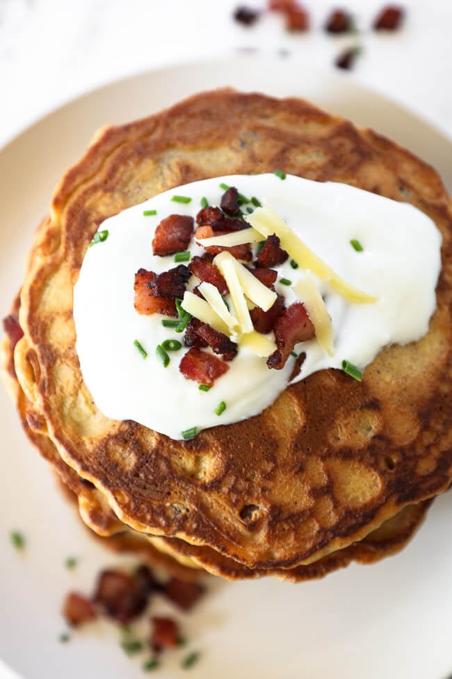 Overhead image of bacon pancake with sour cream, bacon, chives and cheese on top. 