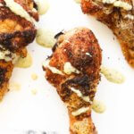 Close up overhead image of baked chicken drumsticks with white sauce drizzled on top