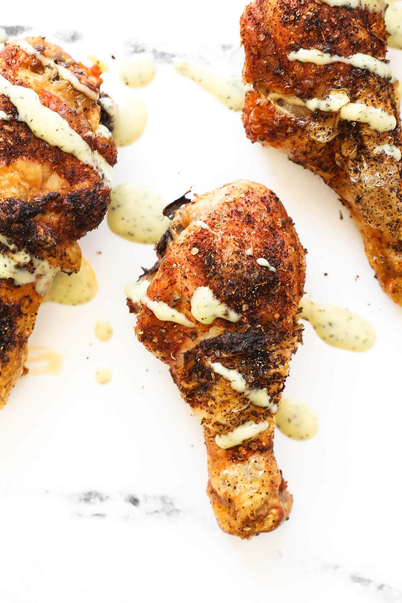 Close up overhead image of baked chicken drumsticks with white sauce drizzled on top