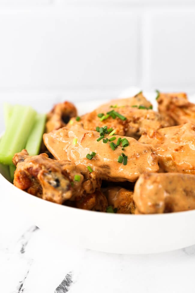 Straight on shot of chicken wings tossed in creamy buffalo sauce with celery sticks